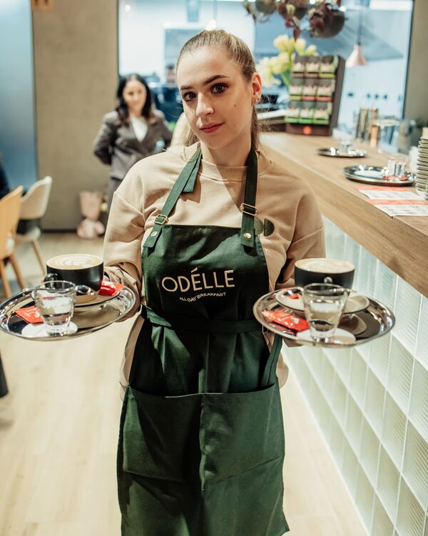 Ospătăriță Odelle cu două tăvi de deserturi și cafea